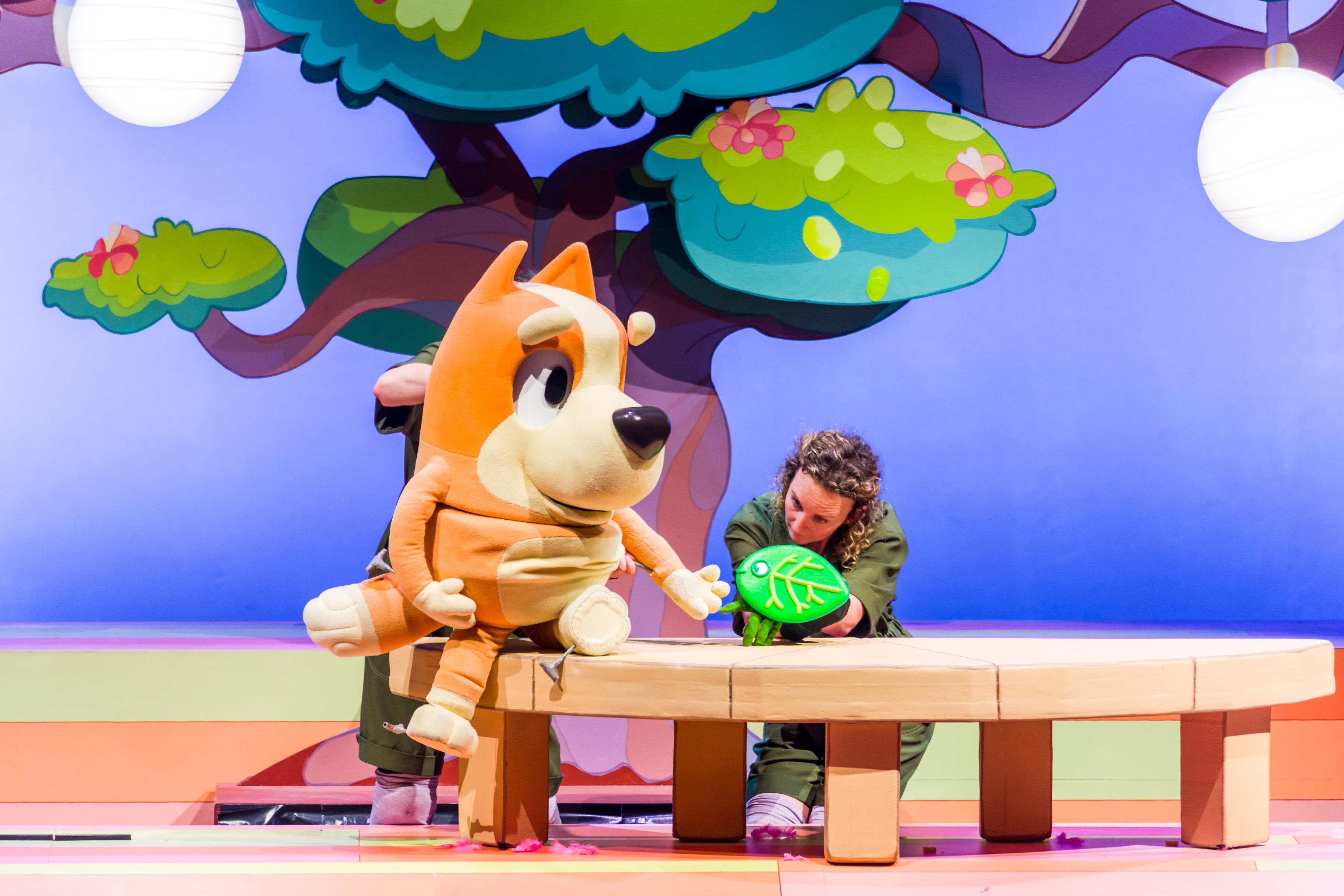 a puppet dog sat beneath a tree with a puppeteer