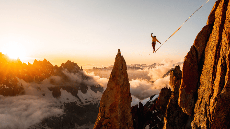 A person tight rope walking between two mountains above the clouds