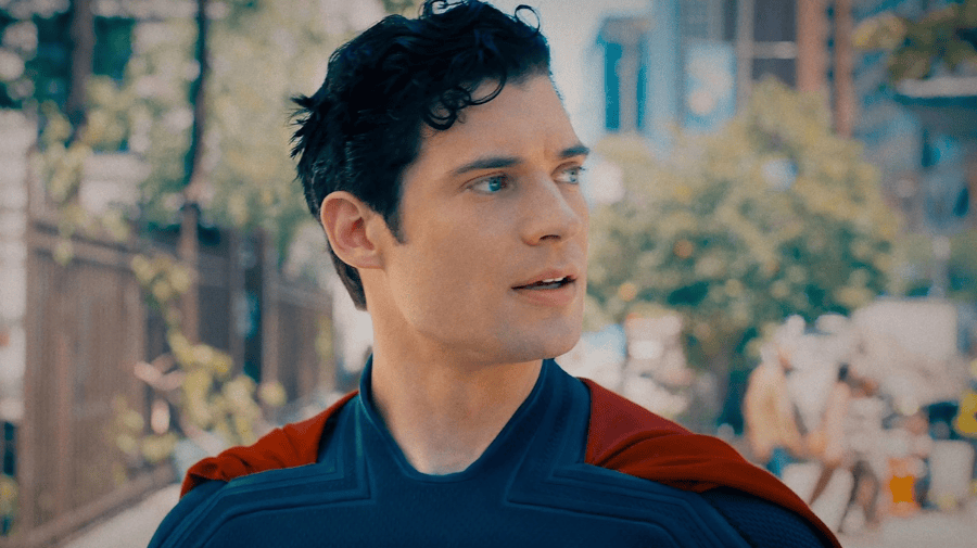 a man with dark short hair is looking to the right of the image. we can see the top of his superhero costume, blue with a red cape 