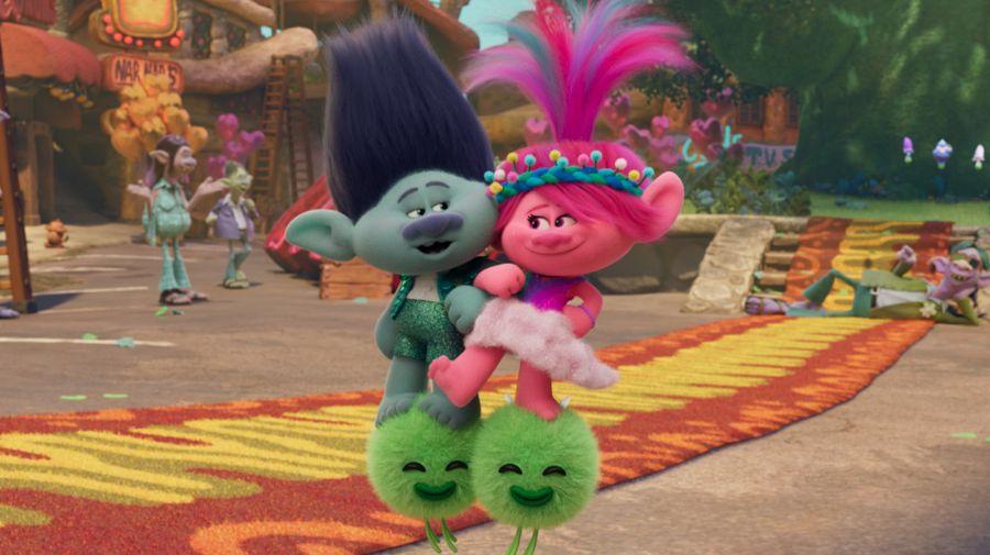 a green troll, Branch, and a pink troll, Poppy, are riding on a pair of fluffy pom poms that have faces on them