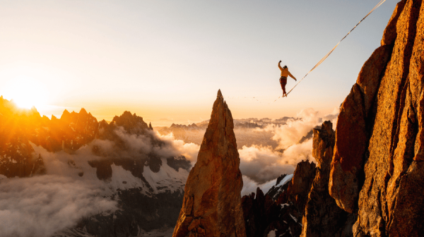 A person tight rope walking between two mountains above the clouds