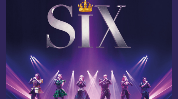six women in clothing of the Tudor times, but spangly, stand confidently holding microphones. above their head is a large silver SIX and a crown instead of a dot on the i 