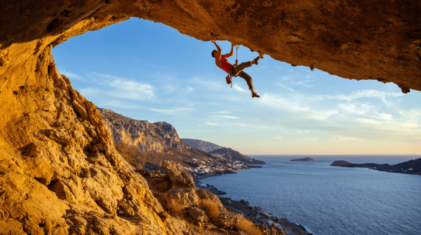 Man climbing a rock face with sea view behind him.