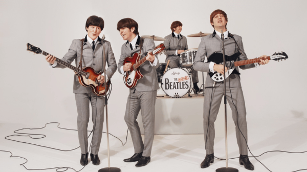 Four men in grey suits holding guitars.