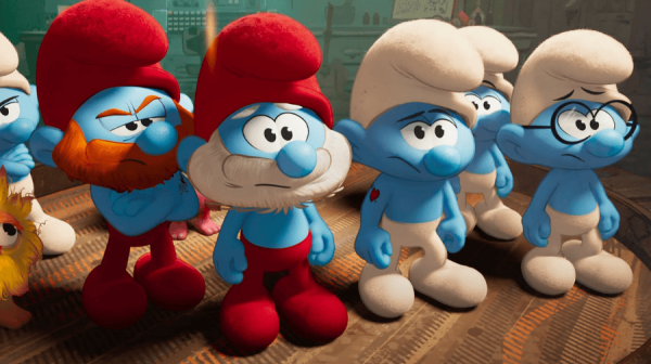 four smurfs, tiny little trolls, that all have blue skin, stand in a line. They have red or white floppy hats o 